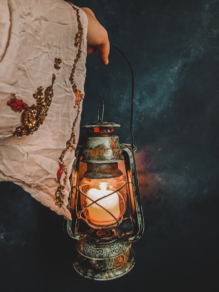 Close-up of a hand holding a vintage lantern with an embroidered sleeve in the dark.